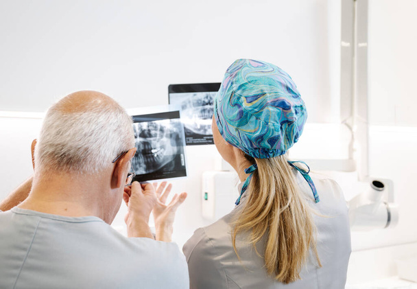 Зворотній перегляд анонімного чоловіка і жінки, які вивчають рентгенівський промінь зубів під час роботи в сучасній клініці разом
 - Фото, зображення