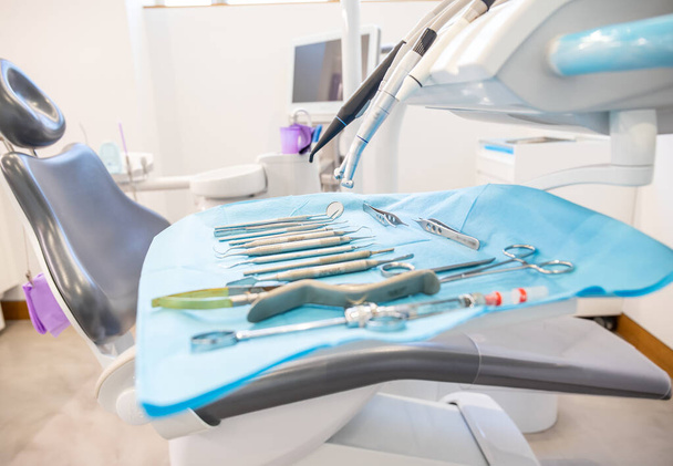 Ensemble d'instruments dentaires propres placés sur une serviette jetable sur une table près d'une chaise au bureau dans une clinique moderne - Photo, image