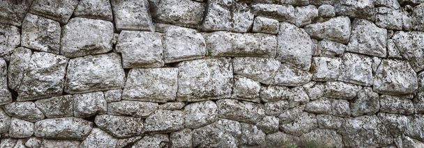 Antigua pared de piedra hecha de piedras ásperas naturales en el estilo mediterráneo. Albañilería antigua sin cemento con una textura labrada de un muro de piedra, formato panorámico para su fondo creativo
. - Foto, imagen