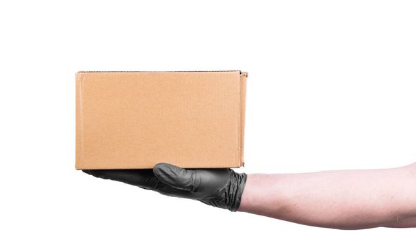 使い捨てブラックグローブの男性の手は段ボール箱を保持しています-白い背景に隔離された商品の安全な配達、コピースペース - 写真・画像