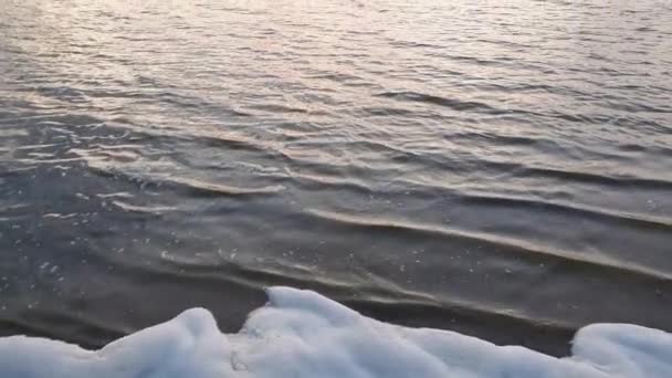 Golden hour, waterscape. Lot of white fluffy foam on the shore of a pond. Surf created by the lake waves, against colorful evening sky. Idyllic scene, peaceful sunset background. - Footage, Video