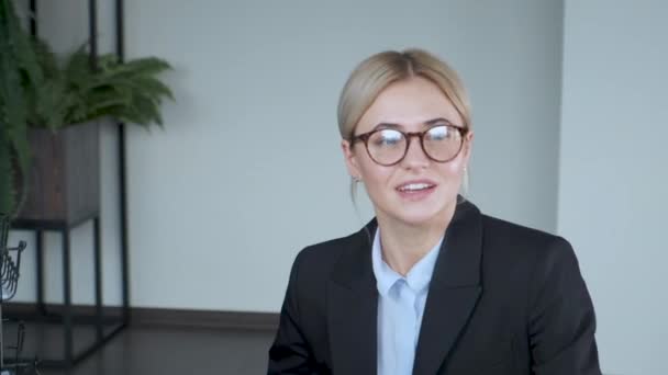 Girl looks into the camera and talks. Communicates. Closeup portrait of smiling businesswoman working at modern office - Materiał filmowy, wideo