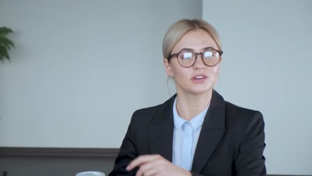 A young business girl tells a story during a break at work, it happens in the office and she has a glass of coffee in her hand - Materiał filmowy, wideo