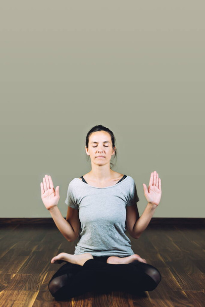Mujer sentada con las piernas cruzadas en el suelo haciendo ejercicios de relajación de yoga
. - Foto, Imagen