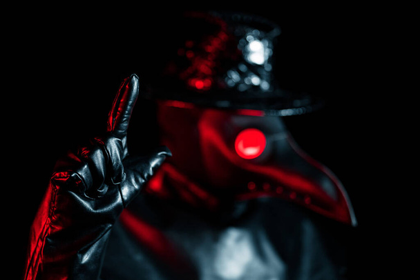 Plague doctor with crow-like mask disapproving with no finger sign, make negation gesture. Denying, Rejecting, Disagree isolated on black background. Creepy mask, historical costume concept. Epidemic - Zdjęcie, obraz