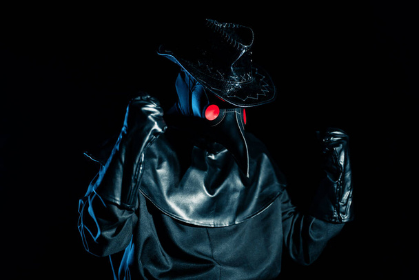 Ο άνθρωπος με κοστούμι γιατρού πανούκλα με κοράκι-όπως μάσκα δείχνει ναι χειρονομία νικητής, χαίρεται απομονώνονται σε μαύρο φόντο. Ανατριχιαστική μάσκα, ιστορική έννοια κοστουμιών. Επιδημία - Φωτογραφία, εικόνα