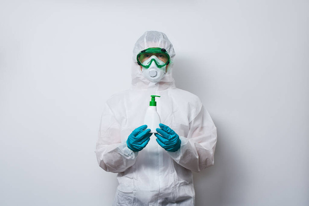 Doctor draagt PPE - kostuum, handschoenen en chirurgische gezichtsmasker in superheld cape met fles antiseptische vloeibare zeep. - Foto, afbeelding