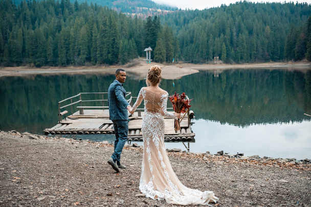 美しい湖の背景にある結婚式で美しい結婚式のカップルの花嫁と新郎。幸せな結婚カップル。結婚式の日に男と女を愛する. - 写真・画像
