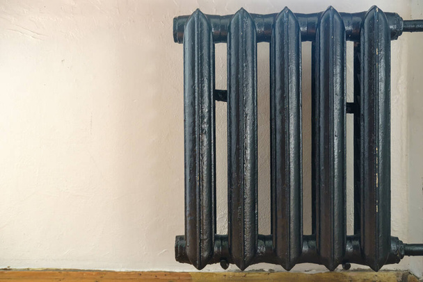 Старый чугунный радиатор, покрашенный в черный цвет на белой стене. Копирование пространства
. - Фото, изображение