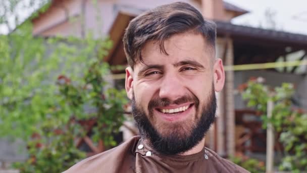 Attractive guy with a large smile after the haircut in the garden at home looking straight to the camera happy and excited - Video, Çekim