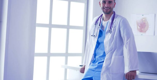 Jovem e confiante retrato médico masculino em pé no consultório médico. - Foto, Imagem