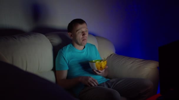 Un uomo solitario trascorre una noiosa serata guardando la TV seduto su un divano e mangiando patatine fritte
 - Filmati, video