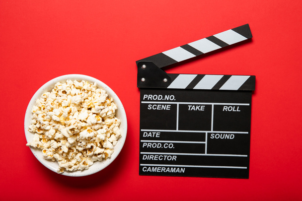 Płyta z popcornem i klapką filmową na czerwonym tle - Zdjęcie, obraz