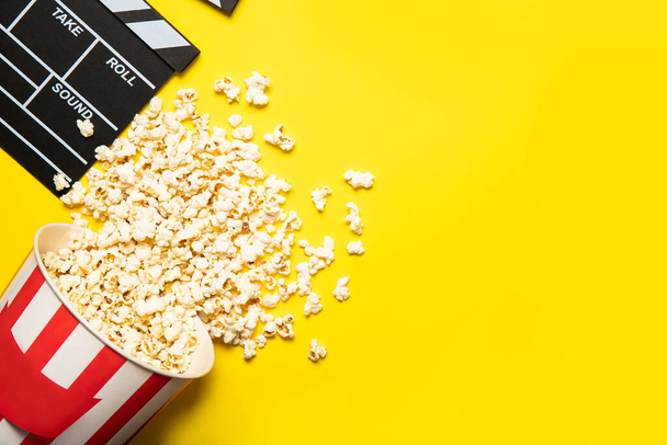 Paper cup with popcorn and movie clapper on a yellow background, place for text - Фото, изображение