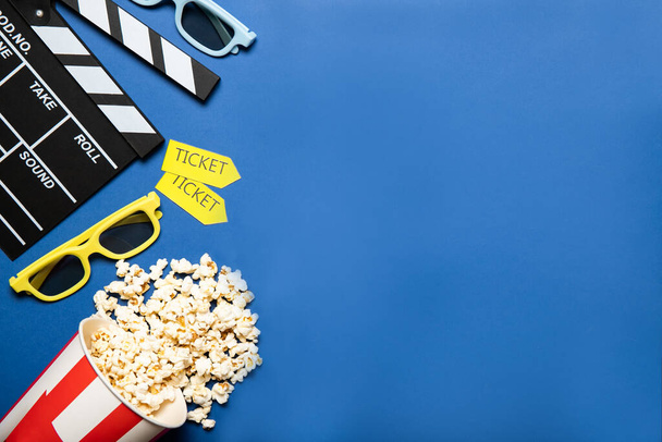 Papieren beker met popcorn en filmklepper op een blauwe achtergrond, plaats voor tekst - Foto, afbeelding