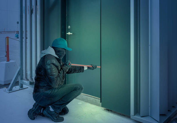 Грабитель в маске и ломе врывается в здание ночью
 - Фото, изображение