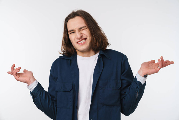 Image of confused young man with long hair grimacing and throwing up hands isolated over white background - Photo, Image
