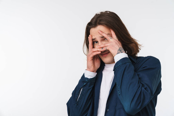 Image of scared young man with long hair looking at camera and covering his face isolated over white background - Fotografie, Obrázek