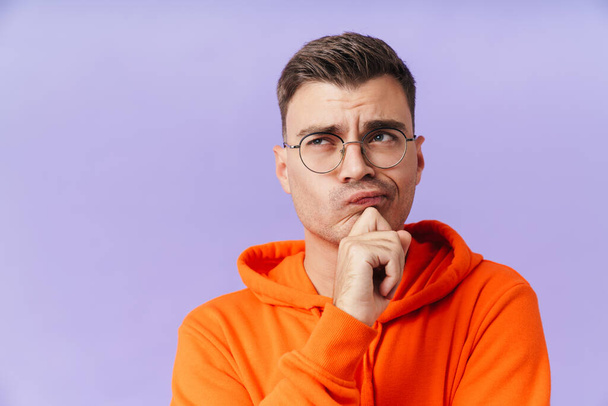 Image of serious thinking young man isolated over purple background wearing eyeglasses looking aside. - Фото, зображення