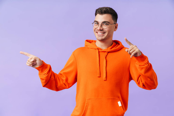 Image of happy positive cheerful young man isolated over purple background wearing eyeglasses pointing. - Photo, Image
