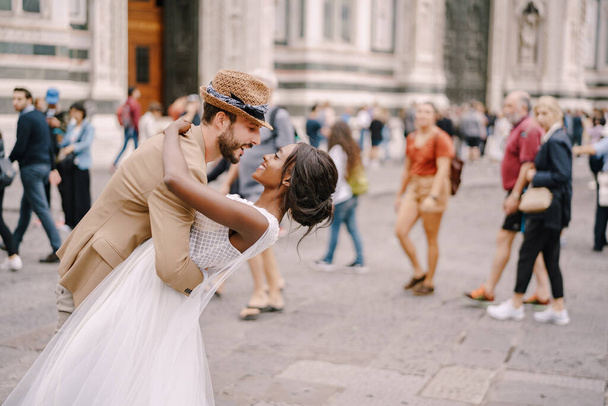 Pareja de boda multiétnica. Boda en Florencia, Italia. Novia afroamericana y novio caucásico abrazándose en Piazza del Duomo
. - Foto, imagen
