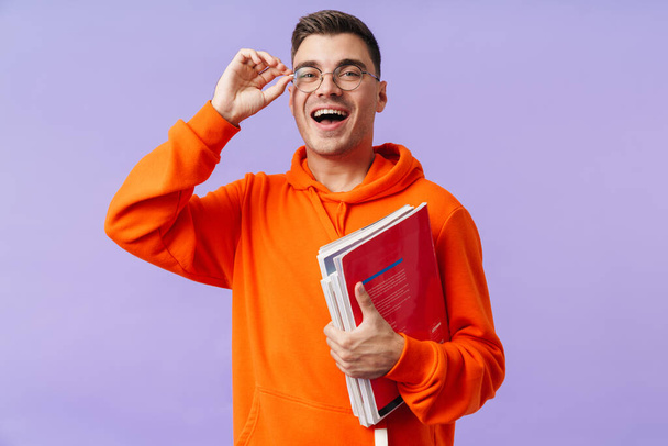 Photo of happy positive young man student posing isolated over purple background holding copybooks. - Foto, immagini