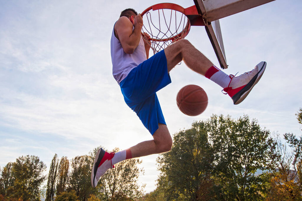 Young man jumping and making a fantastic slam dunk playing streetball, basketball. Urban authentic. - Фото, изображение