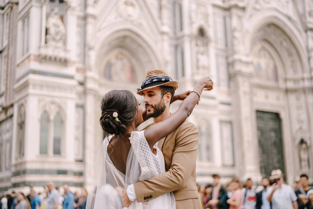 多人種の結婚式のカップル。イタリアのフィレンツェで結婚式。アフリカ系アメリカ人の花嫁とドゥオーモ広場で白人の新郎の抱きしめ. - 写真・画像