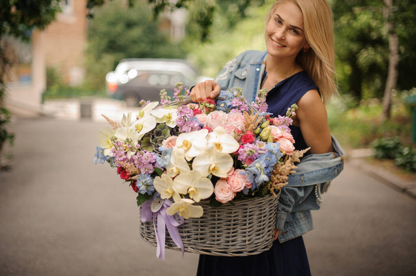 Close-up of woman which holds huge basket with different flowers. - Zdjęcie, obraz