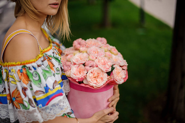Nahaufnahme. Mädchen in buntem Kleid hält sorgfältig runde Schachtel mit frischen rosa Blumen - Foto, Bild