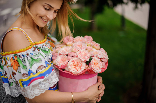 close-up. Smiling blond girl in colorful dress carefully holds round box with flowers - Foto, Imagen