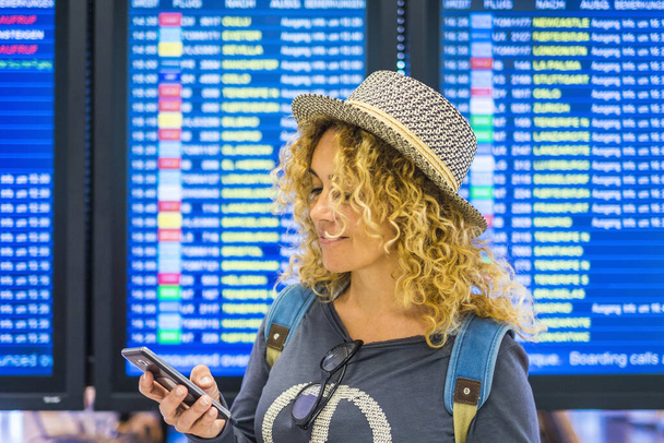 Portré gyönyörű felnőtt nő utazás és ellenőrizze alkalmazás okos telefon elhagyni és kezdeni a repülőtéren - megjeleníti idővel a háttérben - Fotó, kép