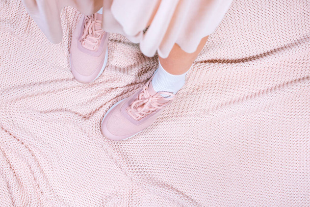 Elegant sporty girl in light transparent, cipher skirt, legs in shoes standing on knitted plaid. Pastel pink color concept. Horizontal photo, above, top view, flat lay. Lifestyle casual fasion - Foto, Imagen