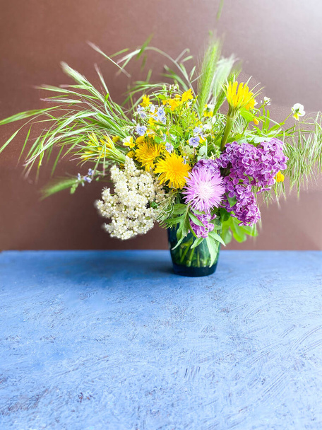 Большой букет ярких разноцветных диких цветов в декоративной вазе на коричневом фоне.
. - Фото, изображение