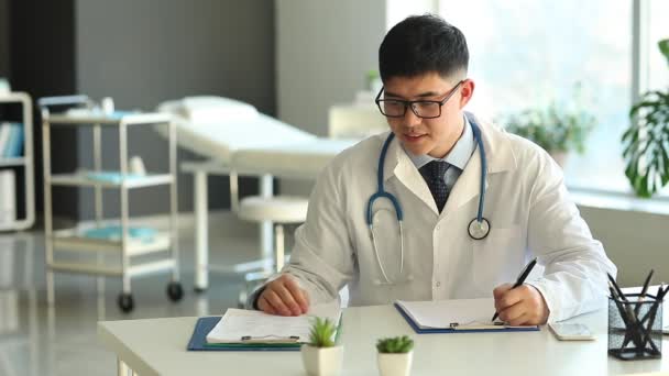 Médico asiático trabajando en la mesa en la clínica
 - Imágenes, Vídeo