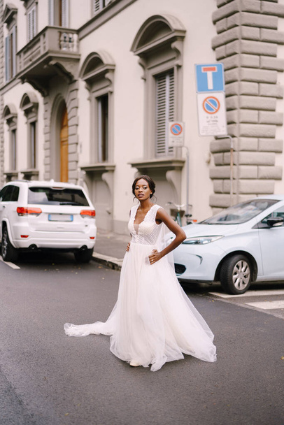 Boda en Florencia, Italia. Novia afroamericana en un vestido blanco, con un largo velo, camina por la carretera en una calle de la ciudad
. - Foto, Imagen