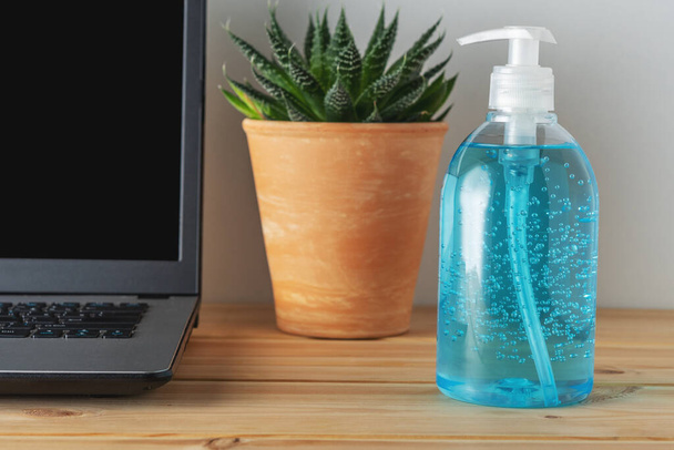 Hand sanitizer in a bottle on wooden table with a laptop. Coronavirus prevention concept. - Foto, Imagem