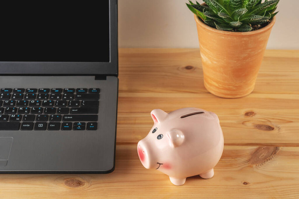 Piggy bank on a wooden table with a laptop. Saving money concept. - Fotoğraf, Görsel