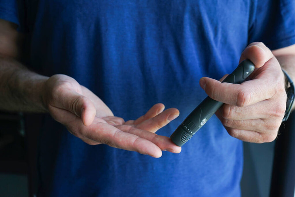 Diabetes-käsite. Miesten kädet, jotka käyttävät lansetia sormella kotona verensokerin tarkistamiseksi, glukometri
,  - Valokuva, kuva