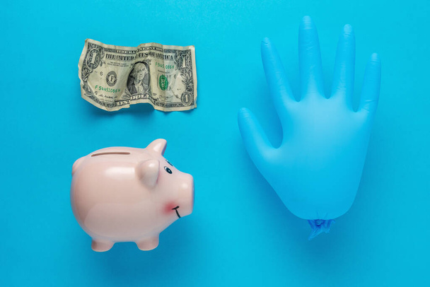 Piggy bank with a medical glove and crumpled dollar bancnote. Minimal Coronavirus outbreak. Saving money concept. - Foto, immagini