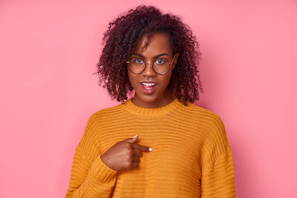 Cute positive young african american female in yellow shirt with glasses points to herself, asks something, has happy expression isolated over pink background. Concept of informed choice - Фото, зображення