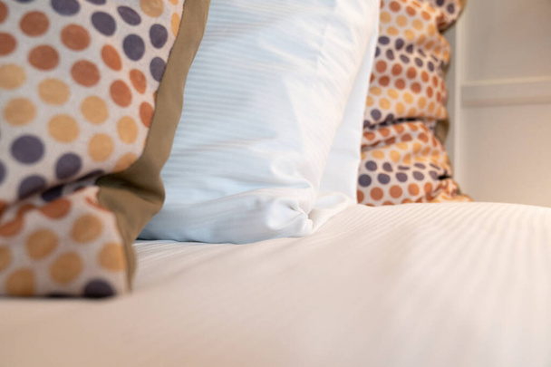 Κόκκινο κίτρινο και γκρι διάστικτο μαξιλάρι διασποράς και ένα λευκό μαξιλάρι ύπνου σε ένα φρέσκο made κρεβάτι στο υπνοδωμάτιο - Φωτογραφία, εικόνα