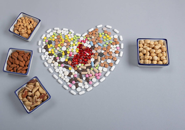 colored pills in the shape of a heart and different types of nuts on a gray background. Traditional medicine and healthy lifestyle concept - Photo, image
