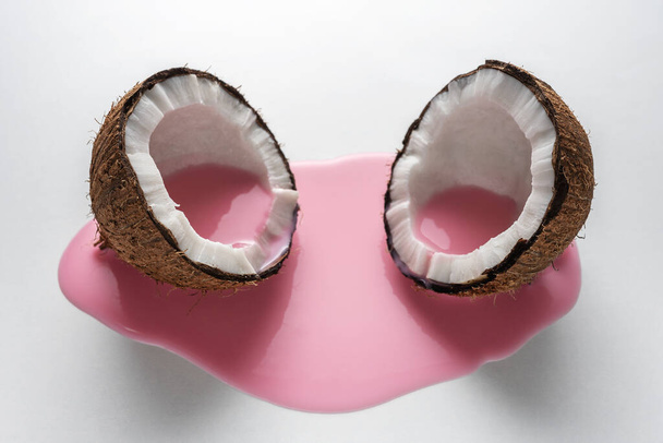 Creative layout made of coconut in half with pink milk pouring. Minimal food concept. - Фото, изображение