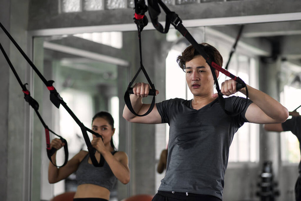Amerikai verejtékes férfi és ázsiai nő tornáznak hasi szíjakkal a fitneszteremben. Testépítő sport és egészséges életmód a boldog párnak. - Fotó, kép