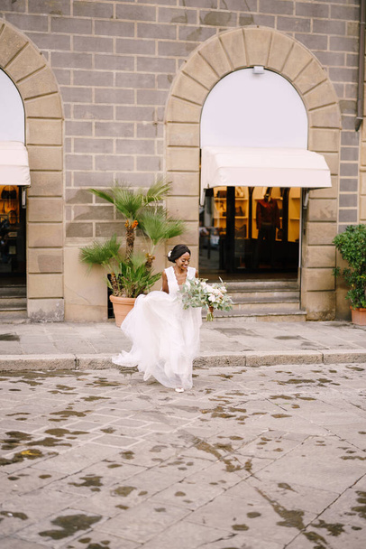 Bruiloft in Florence, Italië. Afro-Amerikaanse bruid in een witte jurk met een lange sluier en een boeket in haar handen. - Foto, afbeelding