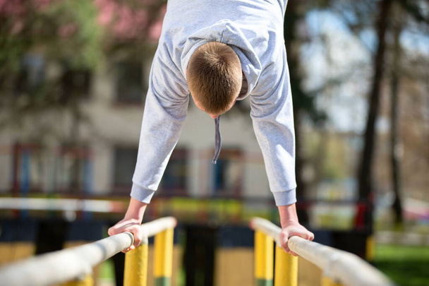 A man is engaged on the uneven bars. Do exercises on the street. - Fotografie, Obrázek