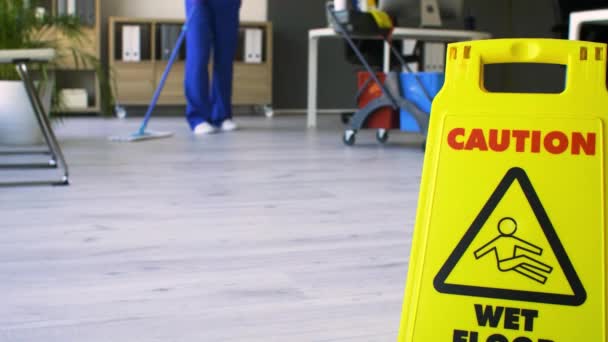 Caution sign with text CAUTION, WET FLOOR and janitor mopping the office - Footage, Video