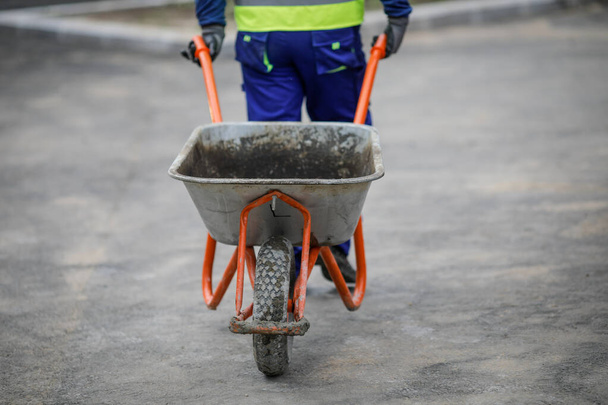 Detalhes com um trabalhador de construção puxando um carrinho de mão em um canteiro de obras
. - Foto, Imagem