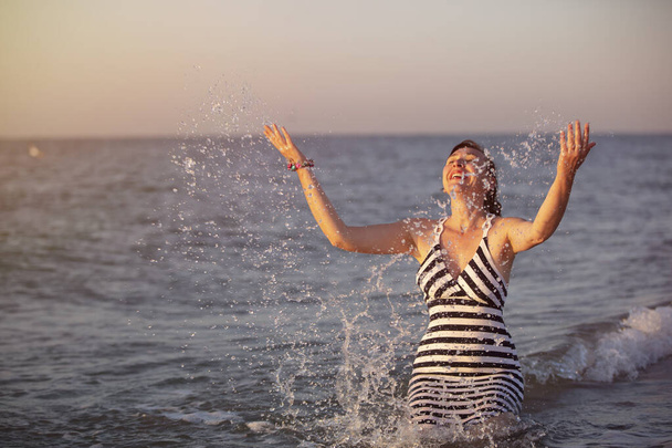 Donna felice sotto il sole sulla riva del mare spruzza acqua.Vacanza al resort. - Foto, immagini